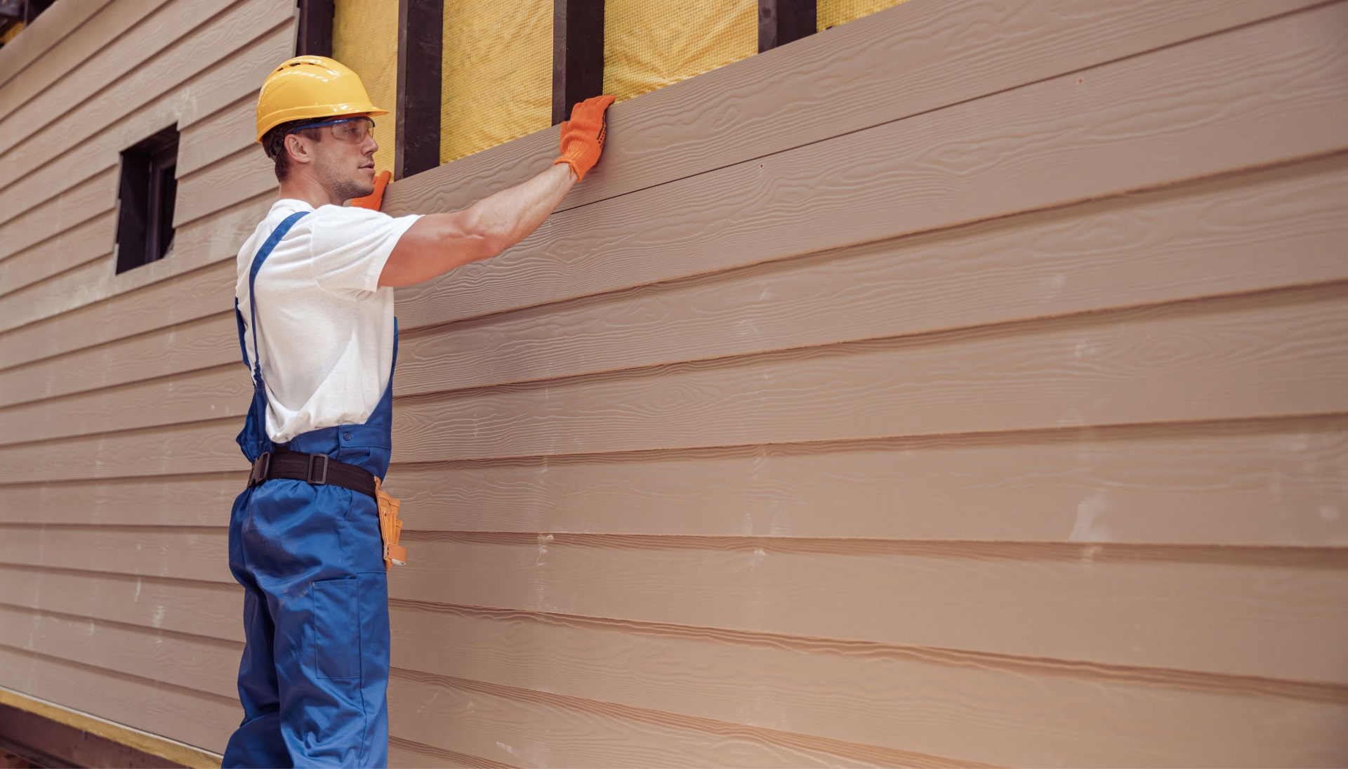 A professional siding contractor wearing a tool belt installs siding on a home in Birmingham, AL.
